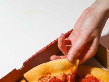 A hand lifting a slice out of the pizza box